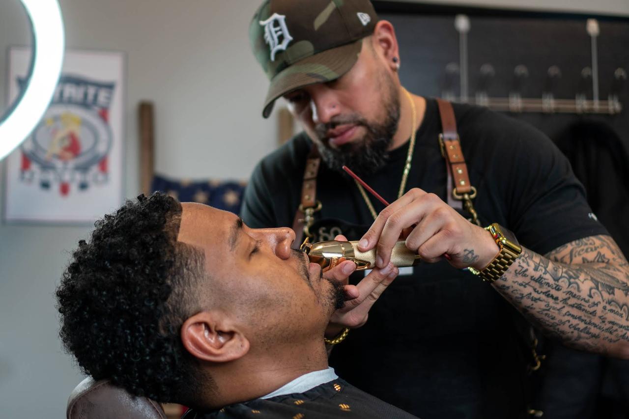 A barber detailing a client’s beard with gold clippers at Social Barber Society in Troy, Michigan